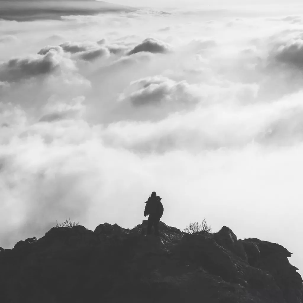 A person on top of a mountain, looking out over clouds.